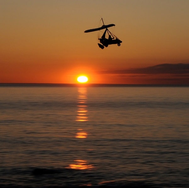 Aerosport Flight Training Flexwing Microlight flying over an ocean sunset